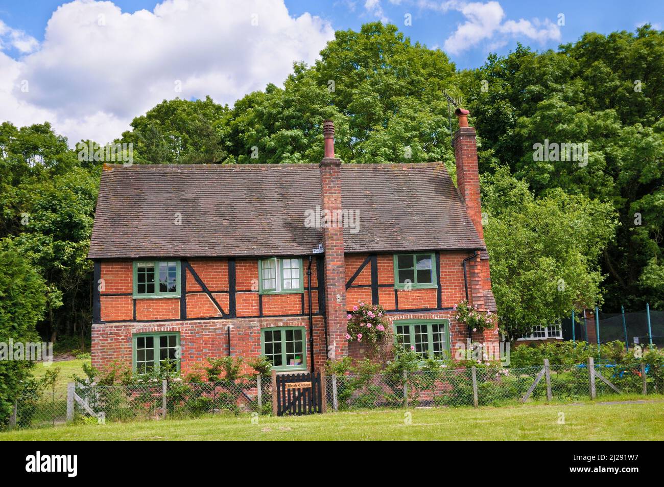Exterior of a charming red brick detached country cottage in summer with pink roses in the village of Shere, Surrey Hills, England, UK Stock Photo