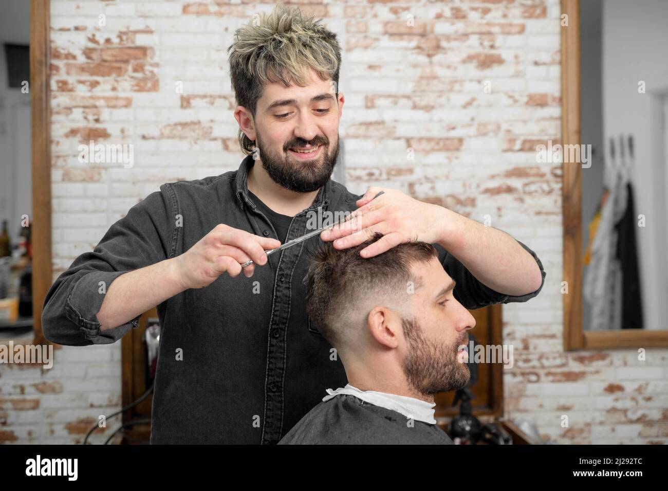 Barber cutting hair with scissors to a handsome young man . High quality photography Stock Photo