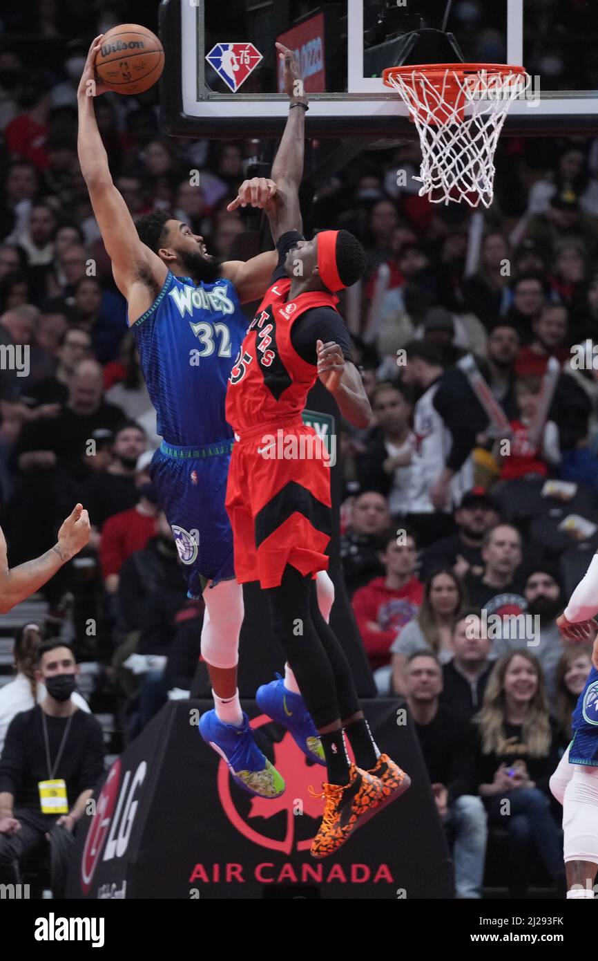 March 30, 2022, TORONTO, ON, CANADA: Minnesota Timberwolves centre  Karl-Anthony Towns (32) dunks the ball past Toronto Raptors forward Chris  Boucher (25) during first half NBA basketball action in Toronto, Wednesday,  March