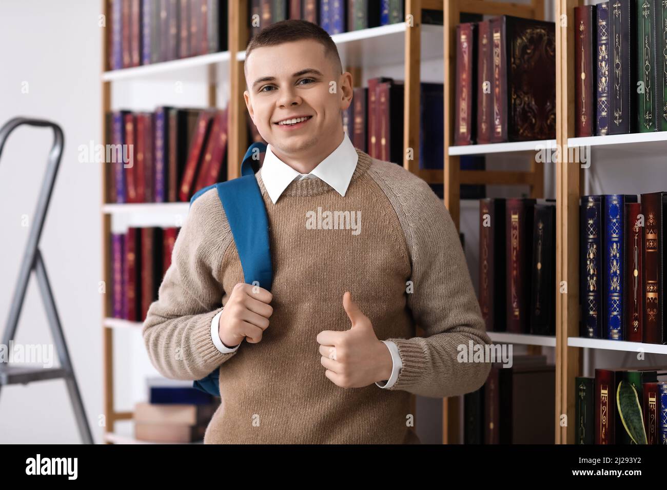 Male student showing thumb-up near bookshelf in library Stock Photo - Alamy