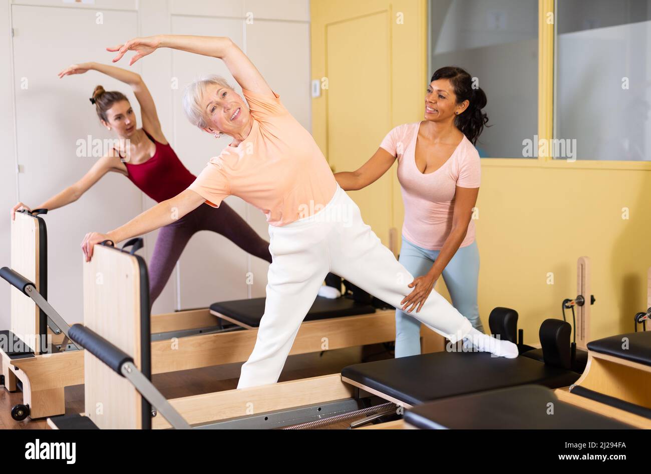 Pilates instructor assisting elderly woman to do exercises on reformer