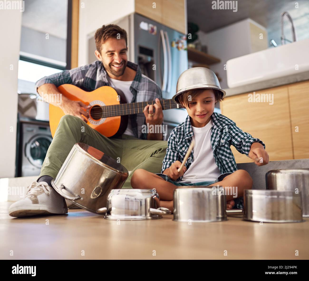 Its a father-son collaboration. Shot of a happy father accompanying his young son on the guitar while he drums on a set of cooking pots. Stock Photo
