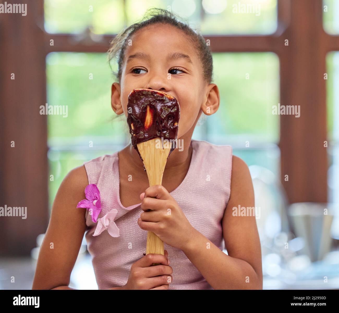 Best morning ever. Shot of an adorable little girl licking a chocolate batter covered spoon while baking in the kitchen at home. Stock Photo