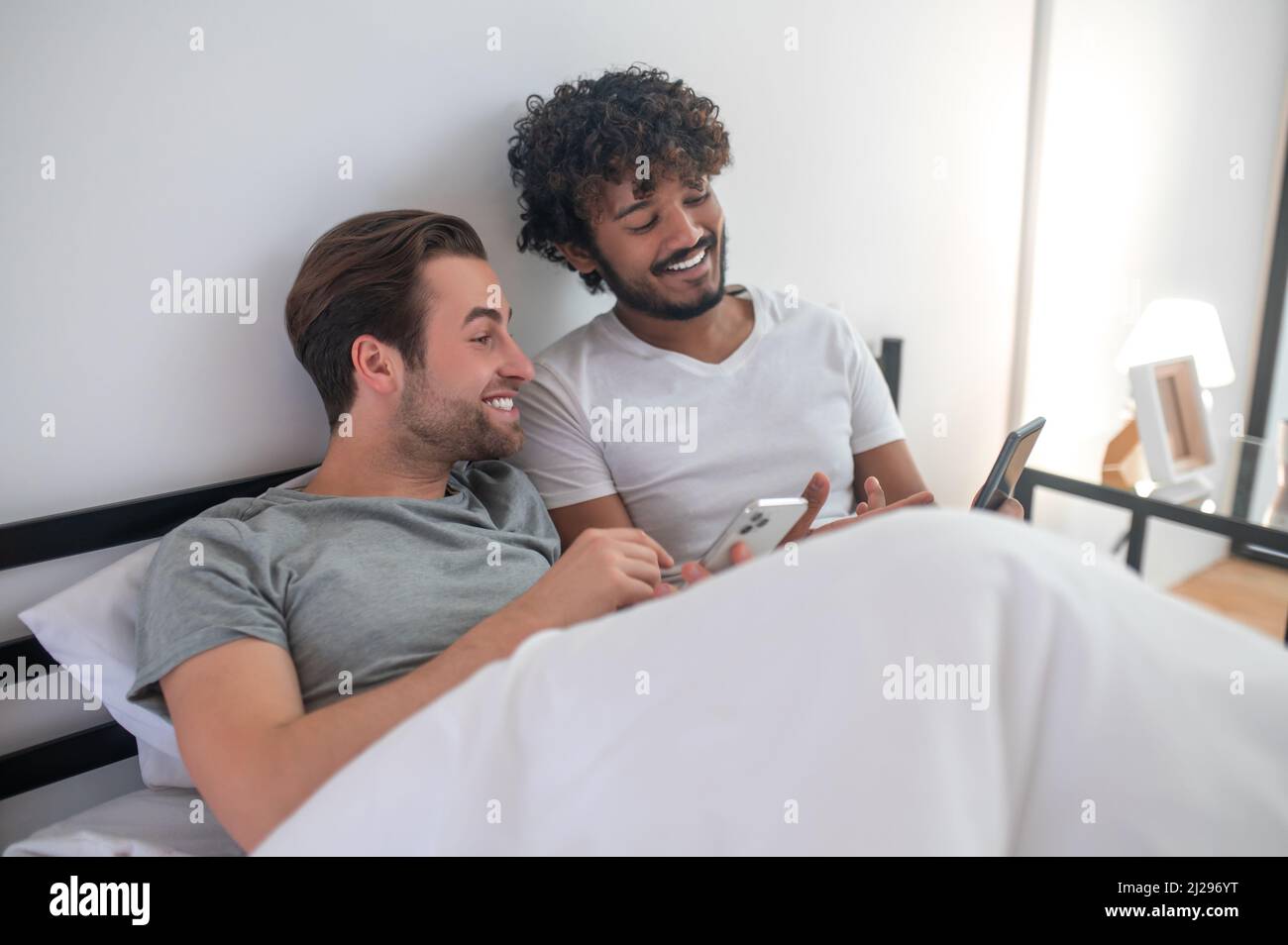 Gay couple using their gadgets in the bedroom Stock Photo