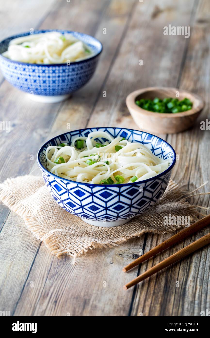 Bowls of noodles on a wooden table, garnished with green onion. Stock Photo