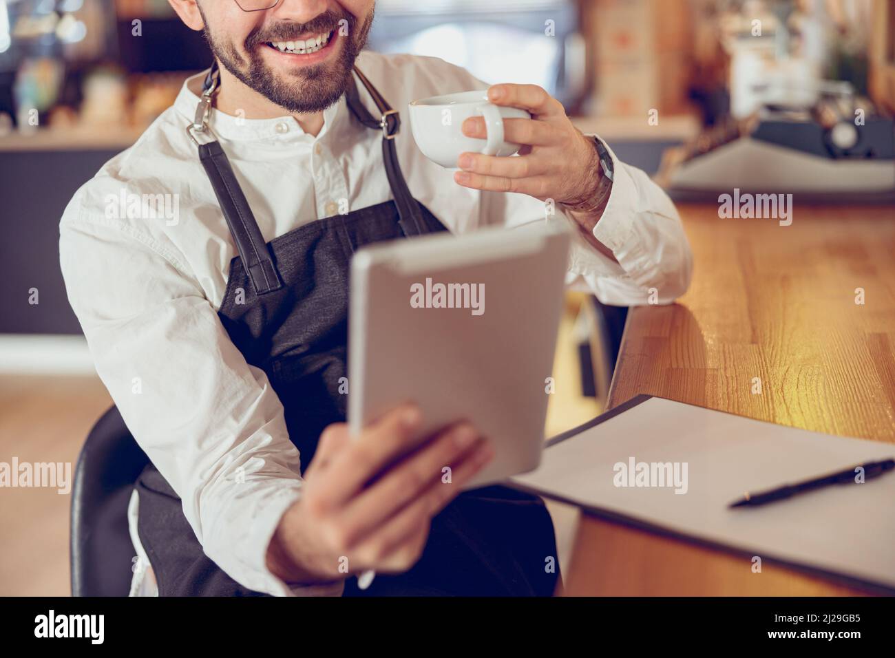 Cheerful man drinking coffee and using tablet computer in cafe Stock Photo