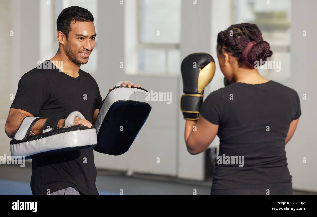 Pack some power into those punches. Shot of a young man training a client in a boxing gym. Stock Photo