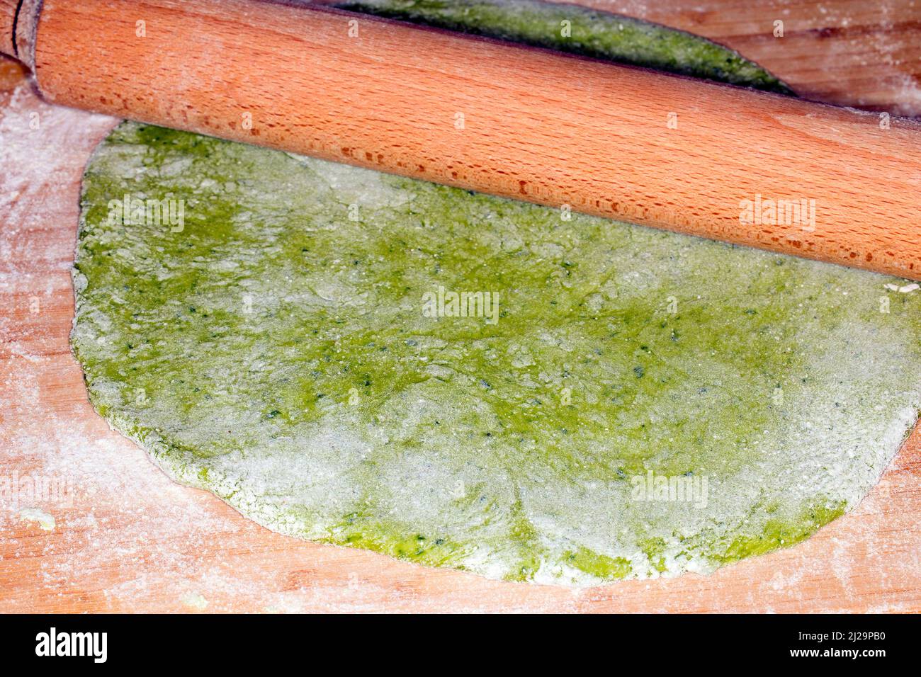 Pasta dough with spinach, is rolled out with a rolling pin Stock Photo