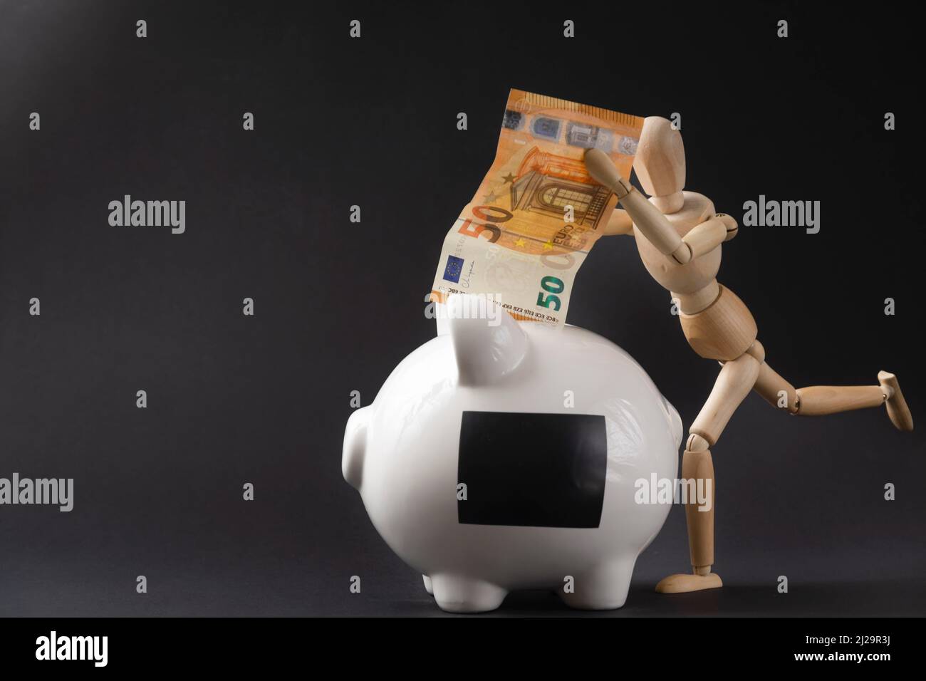 Piggy bank and a mannequin happily throwing a banknote into it Stock Photo