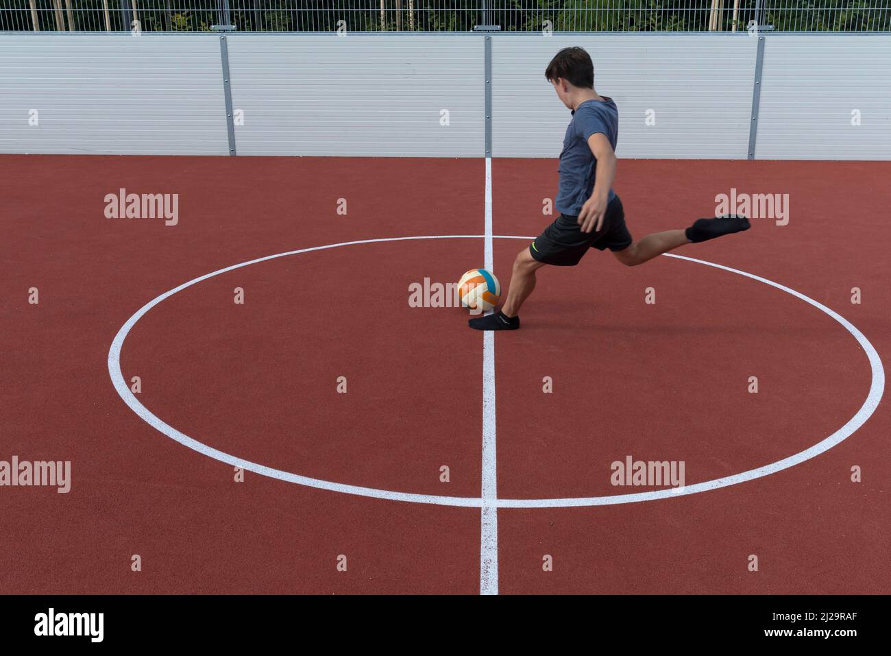 Boy kicks a ball in a football cage, Bavaria, Germany Stock Photo