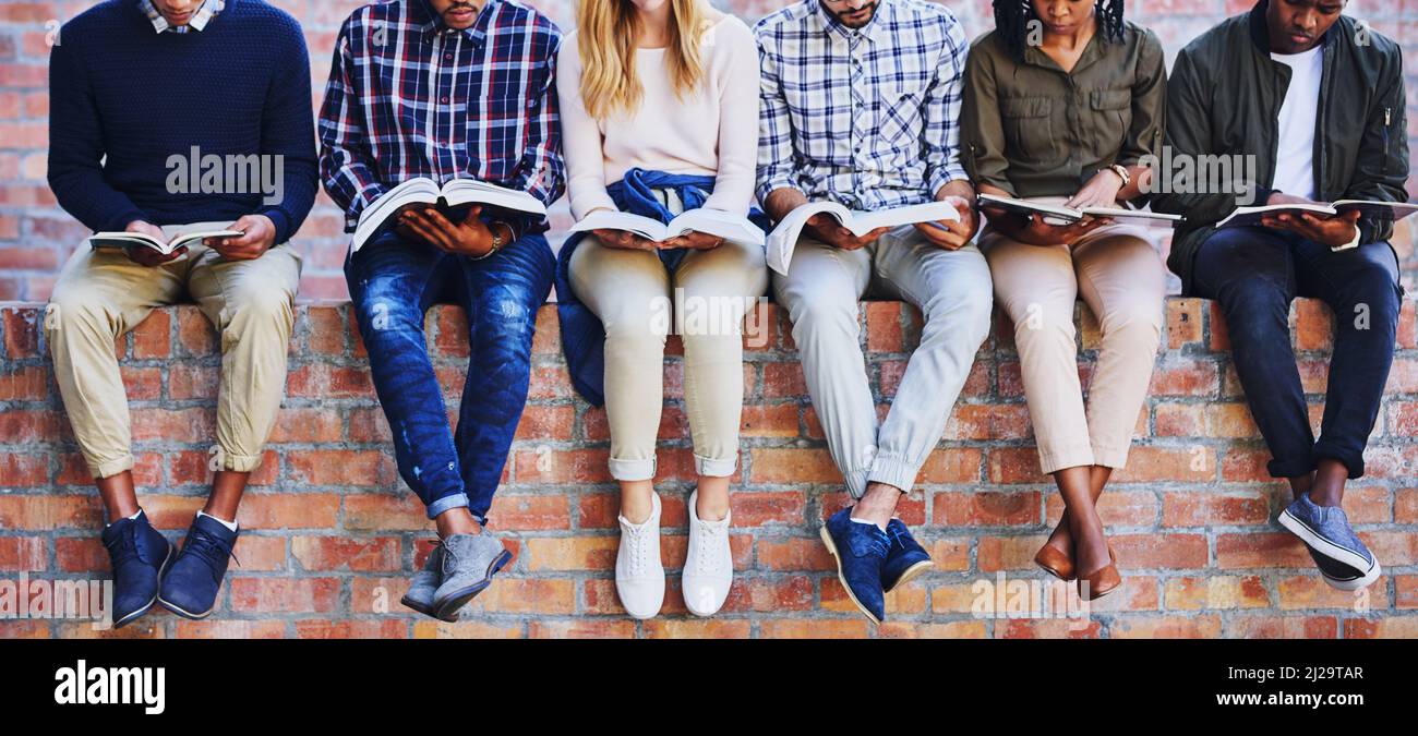 Studying on campus. Cropped shot of a group of unrecognizable university students studying while sitting outside on a facebrick wall. Stock Photo