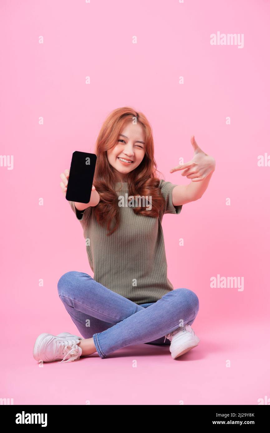 Young Asian woman sitting and using smartphone on pink background Stock ...