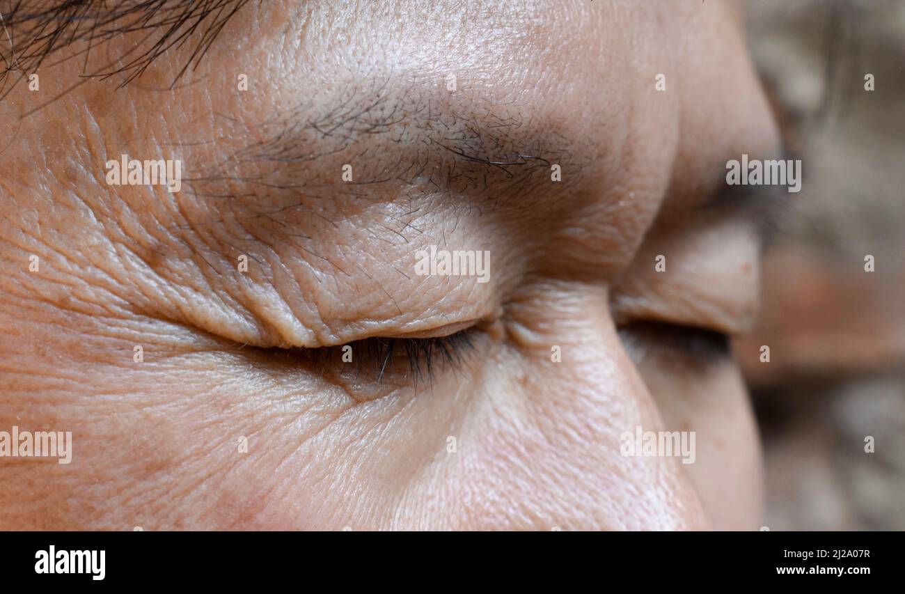 Wrinkles around closed eye of Asian elder man. Closeup view. Stock Photo