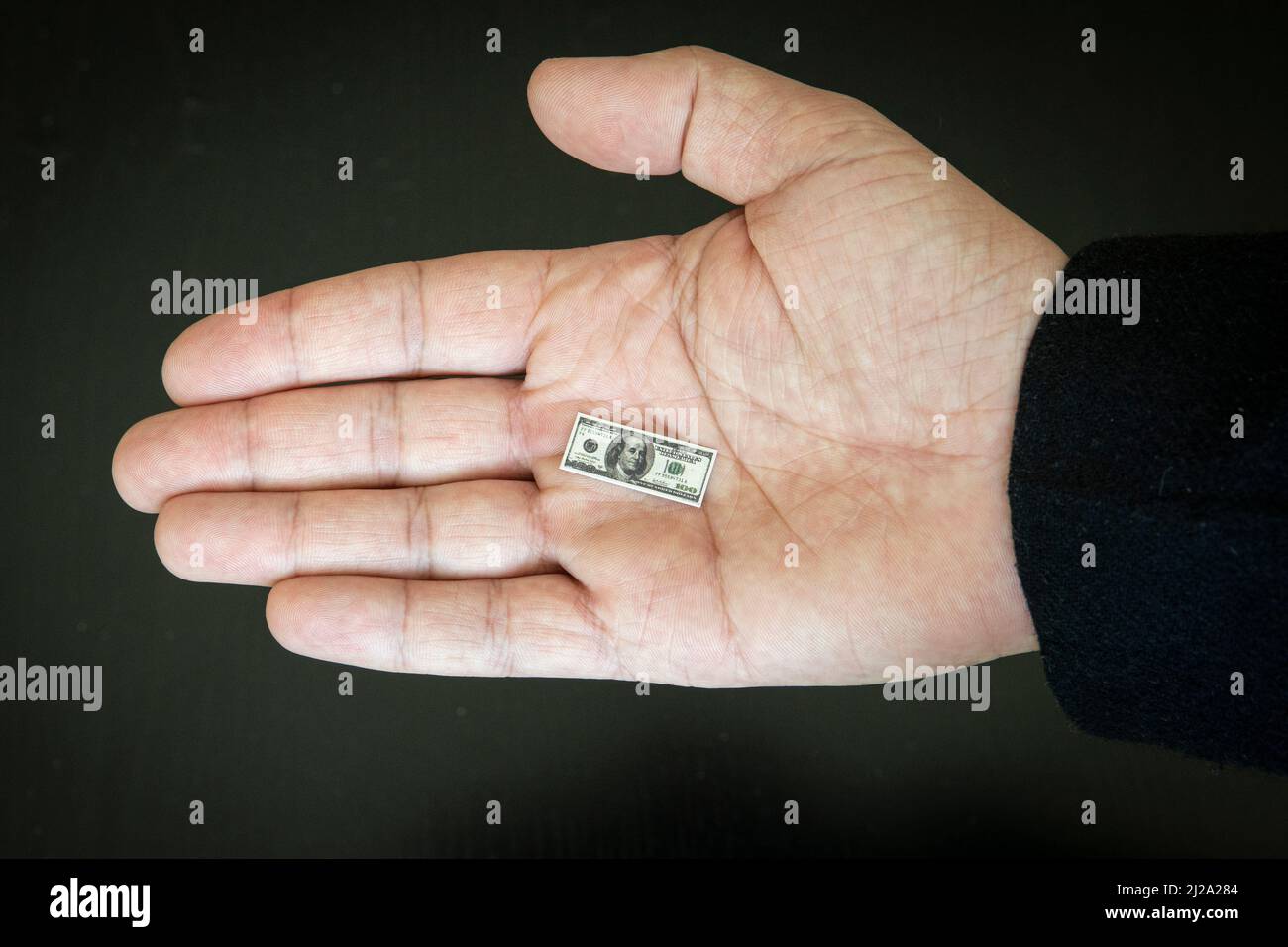 the concept of inflation and falling incomes. a small hundred-dollar bill in the businessman's hand Stock Photo
