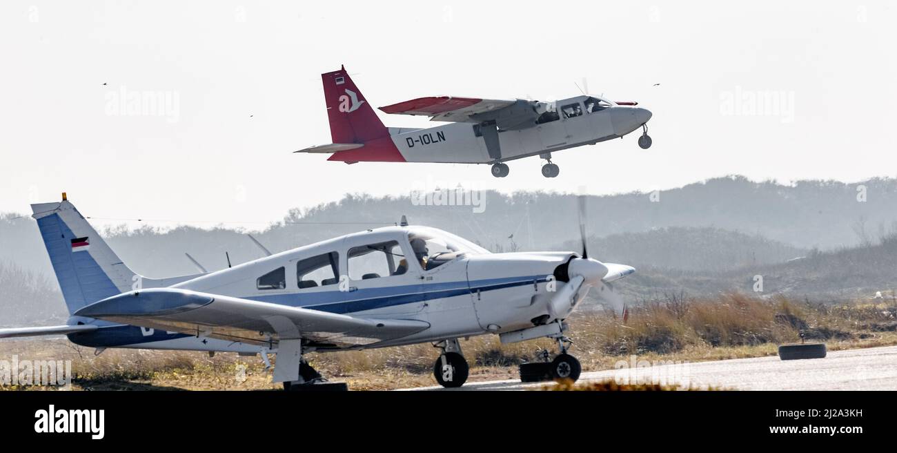 Helgoland, Germany. 25th Mar, 2022. A private aircraft warms up on an apron of the airfield on the Helgoland dune, while a scheduled flight of the Ostfriesischer Flug-Dienst (OFD) takes off in the background. Credit: Markus Scholz/dpa/Alamy Live News Stock Photo