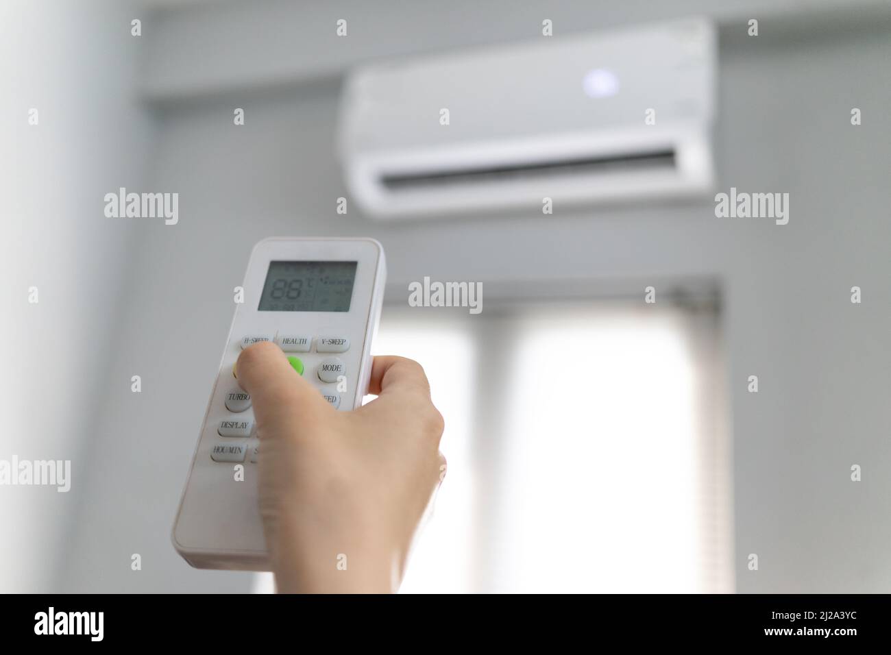 Woman adjusts air conditioning temperature with control Stock Photo Alamy