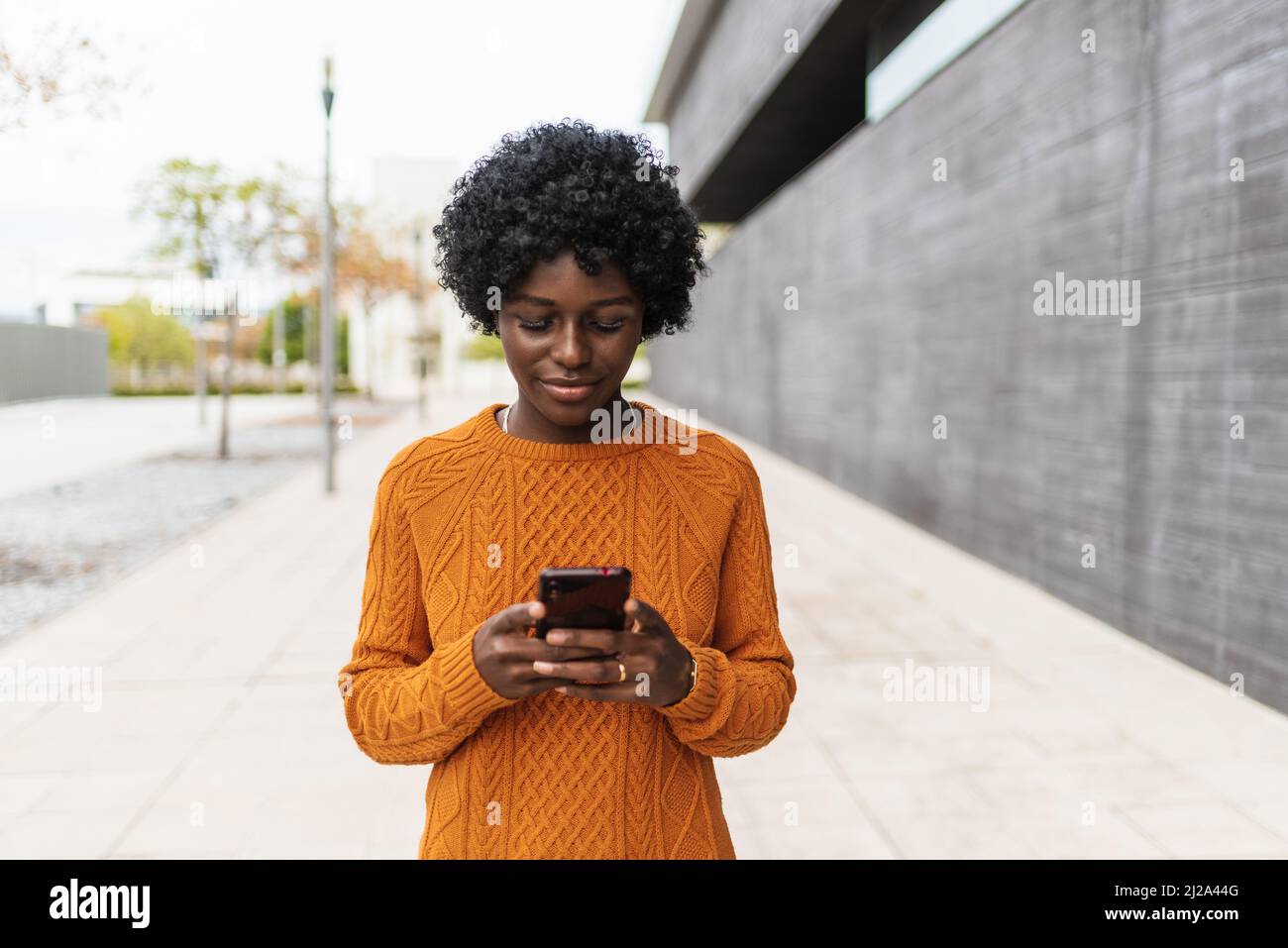 African woman using a smartphone while walking outdoors on the street. Stock Photo