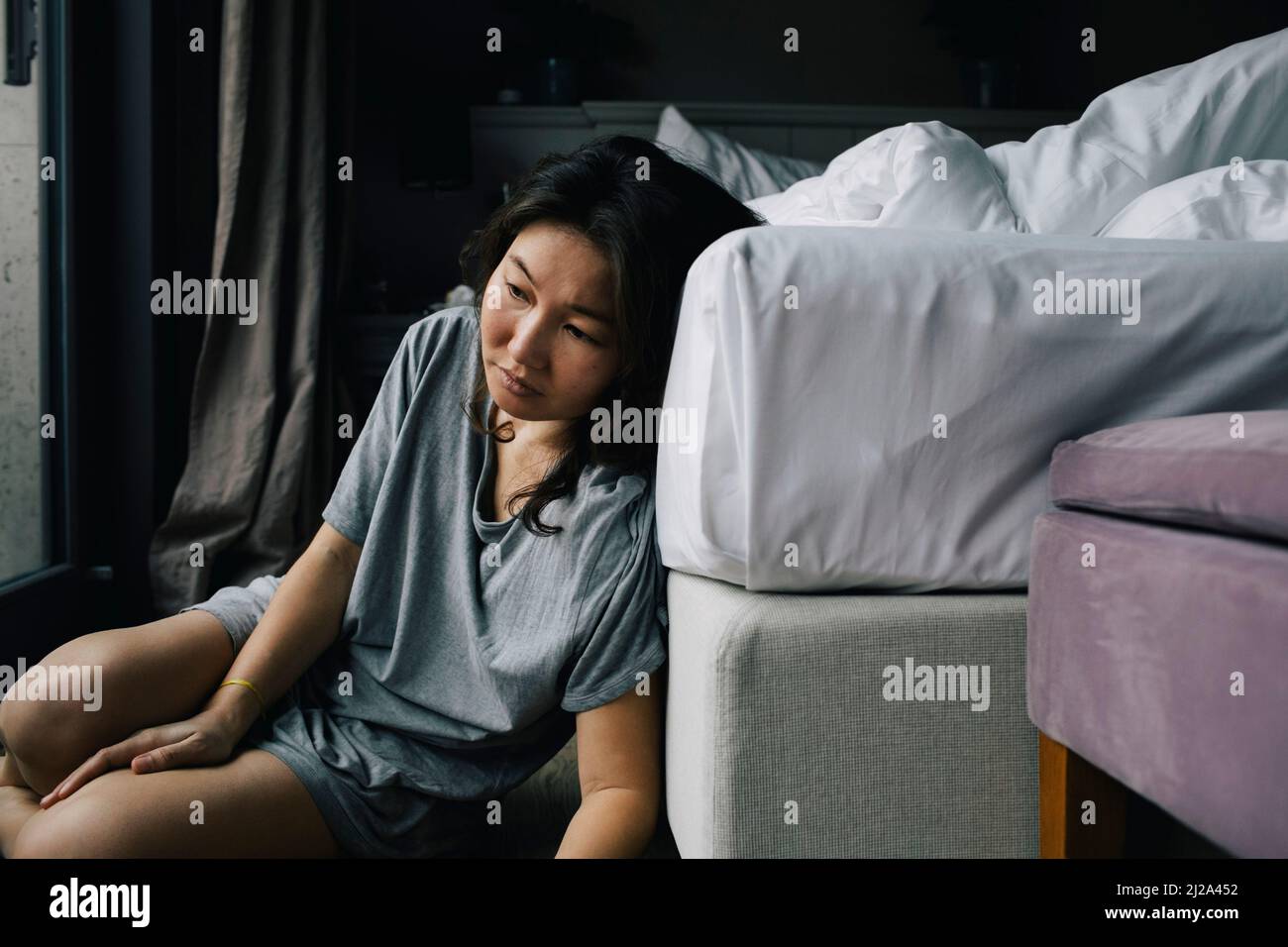 Sad woman with mental disorder leaning on bed at home Stock Photo