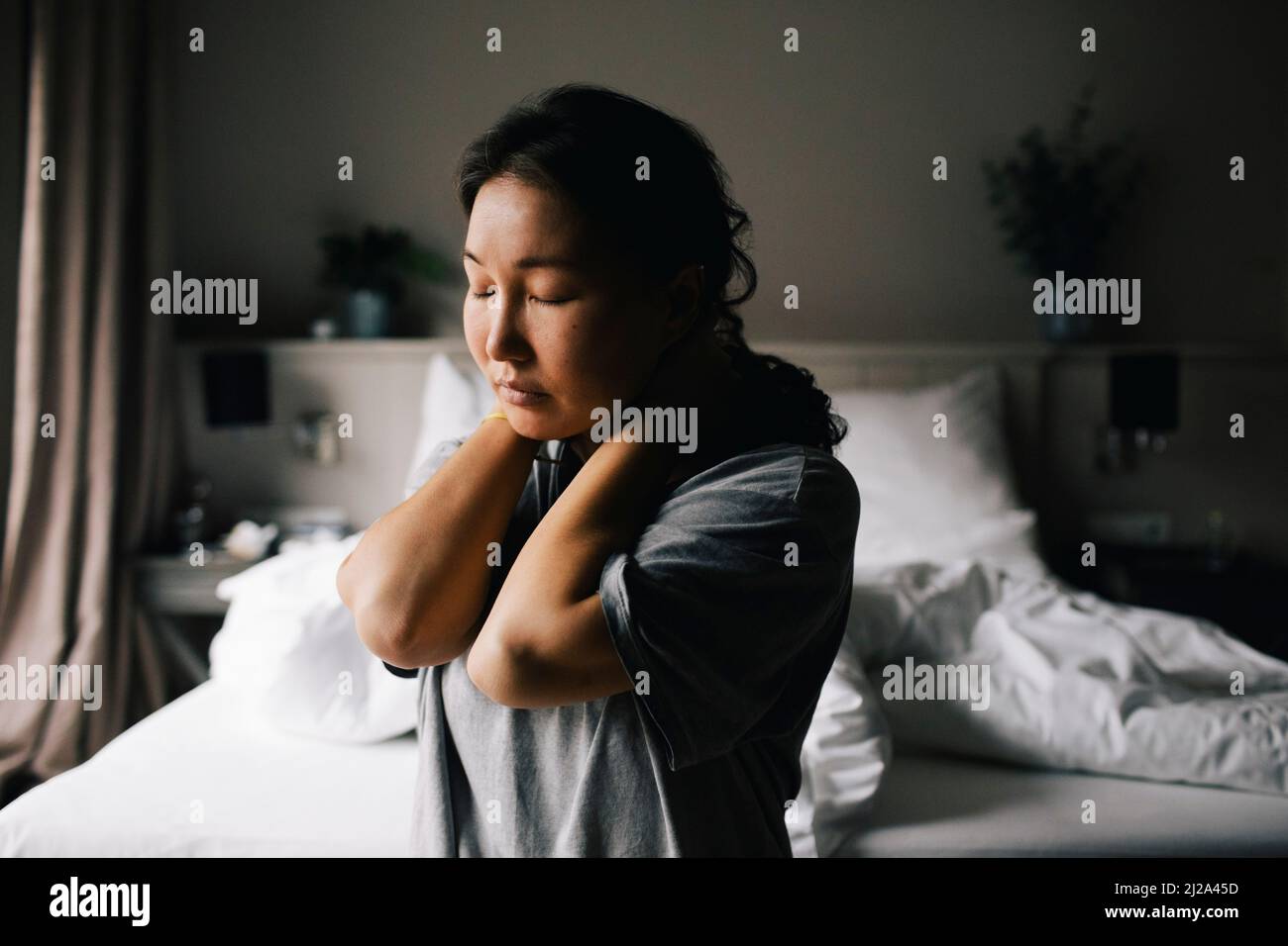 Depressed woman sitting with eyes closed against bed at home Stock Photo
