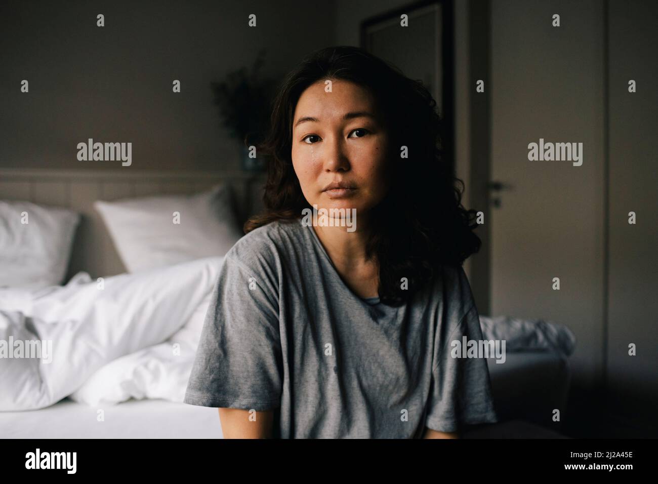 Portrait of sad woman with mental health illness sitting in bedroom at home Stock Photo