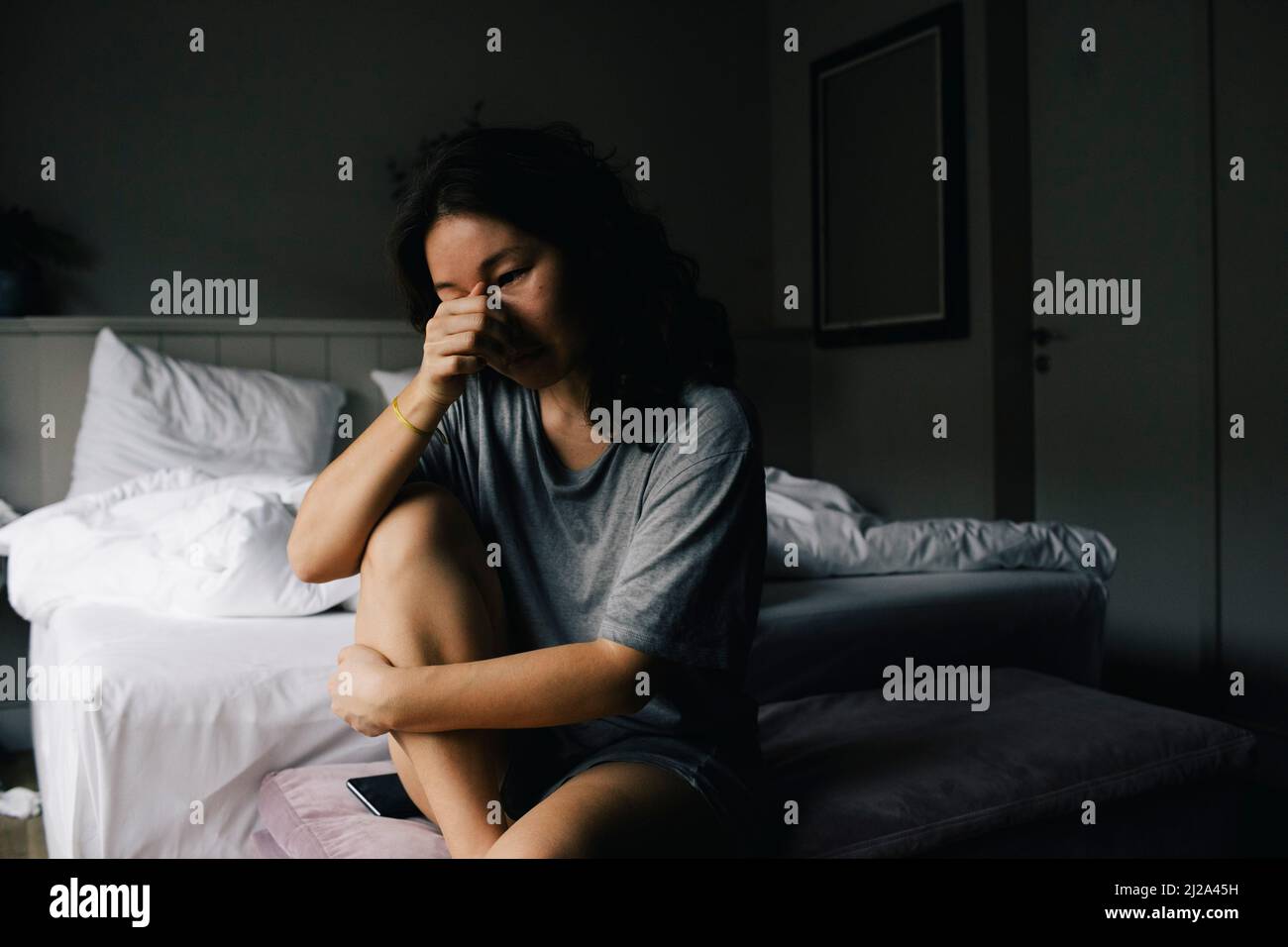 Sad woman crying while sitting on bed end bench in bedroom at home ...