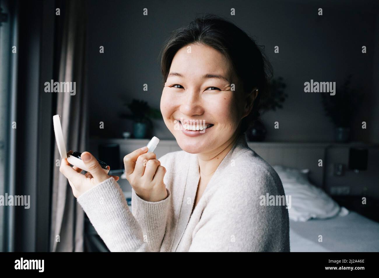 Portrait of happy woman applying make-up in bedroom at home Stock Photo