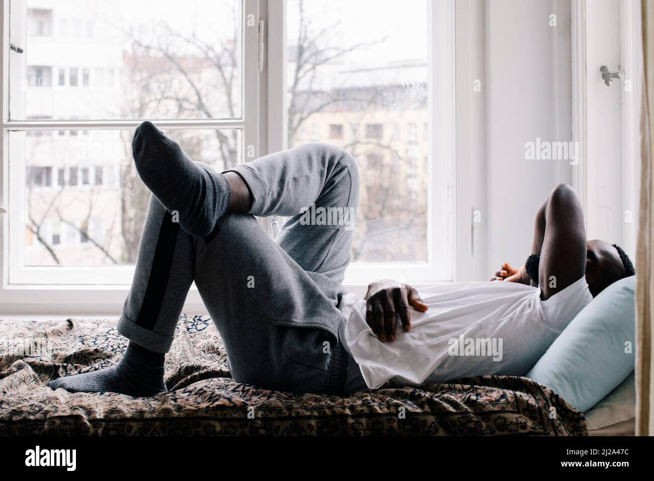 Full length side view of exhausted man sleeping on bed at home Stock
