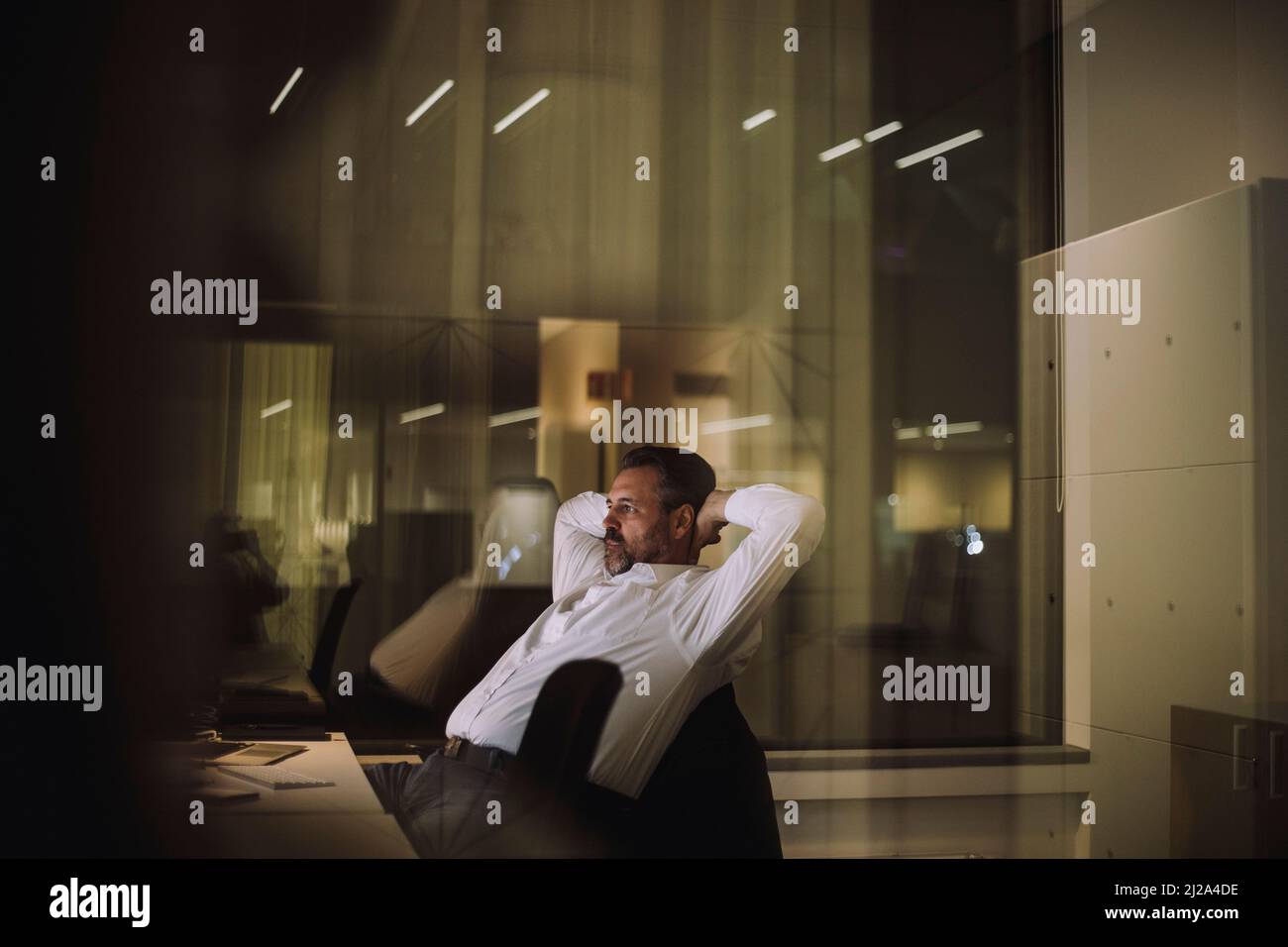 Mature businessman with hands behind head sitting in office at night Stock Photo