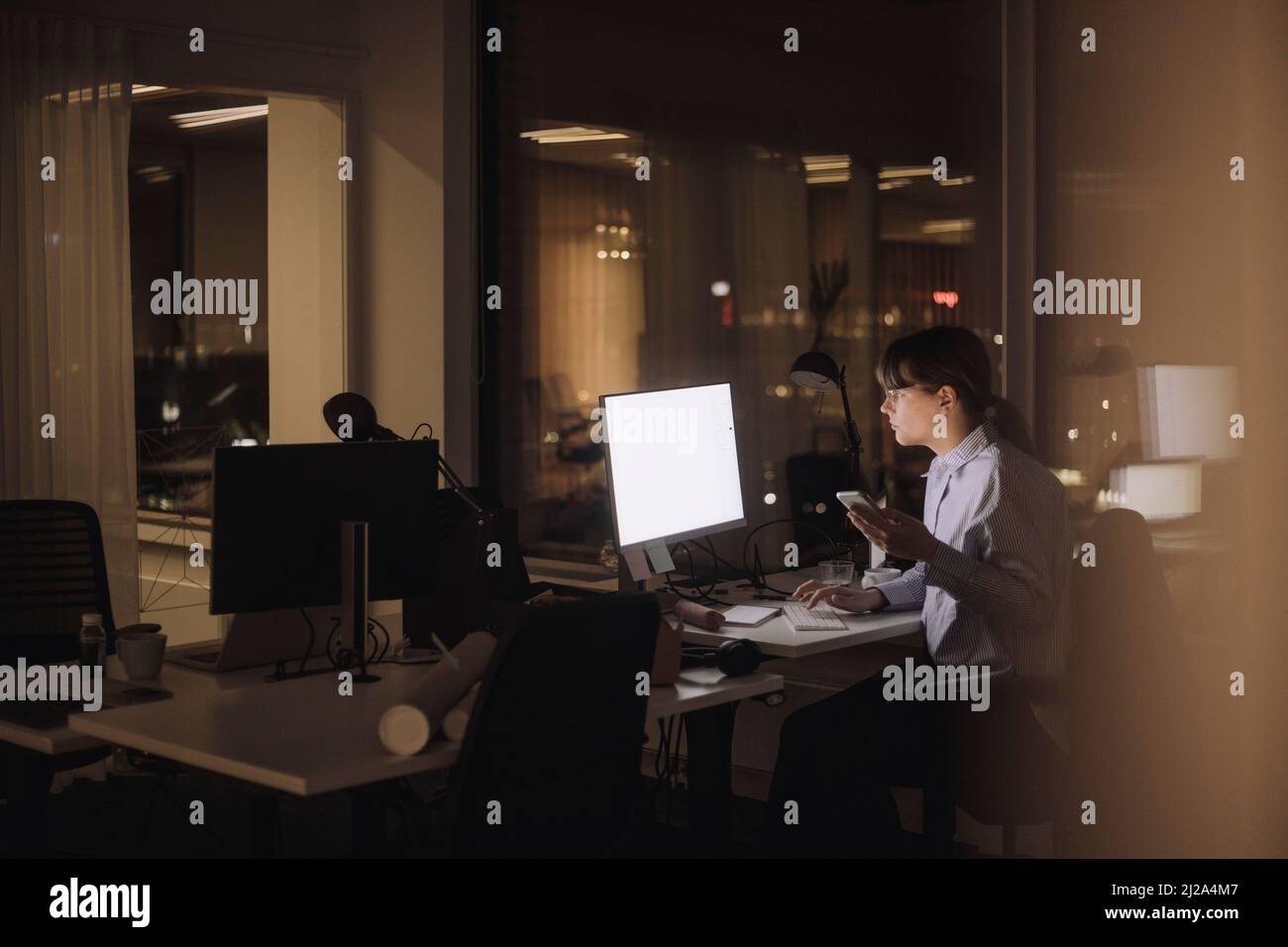 Young businesswoman with smart phone using computer at work place Stock Photo