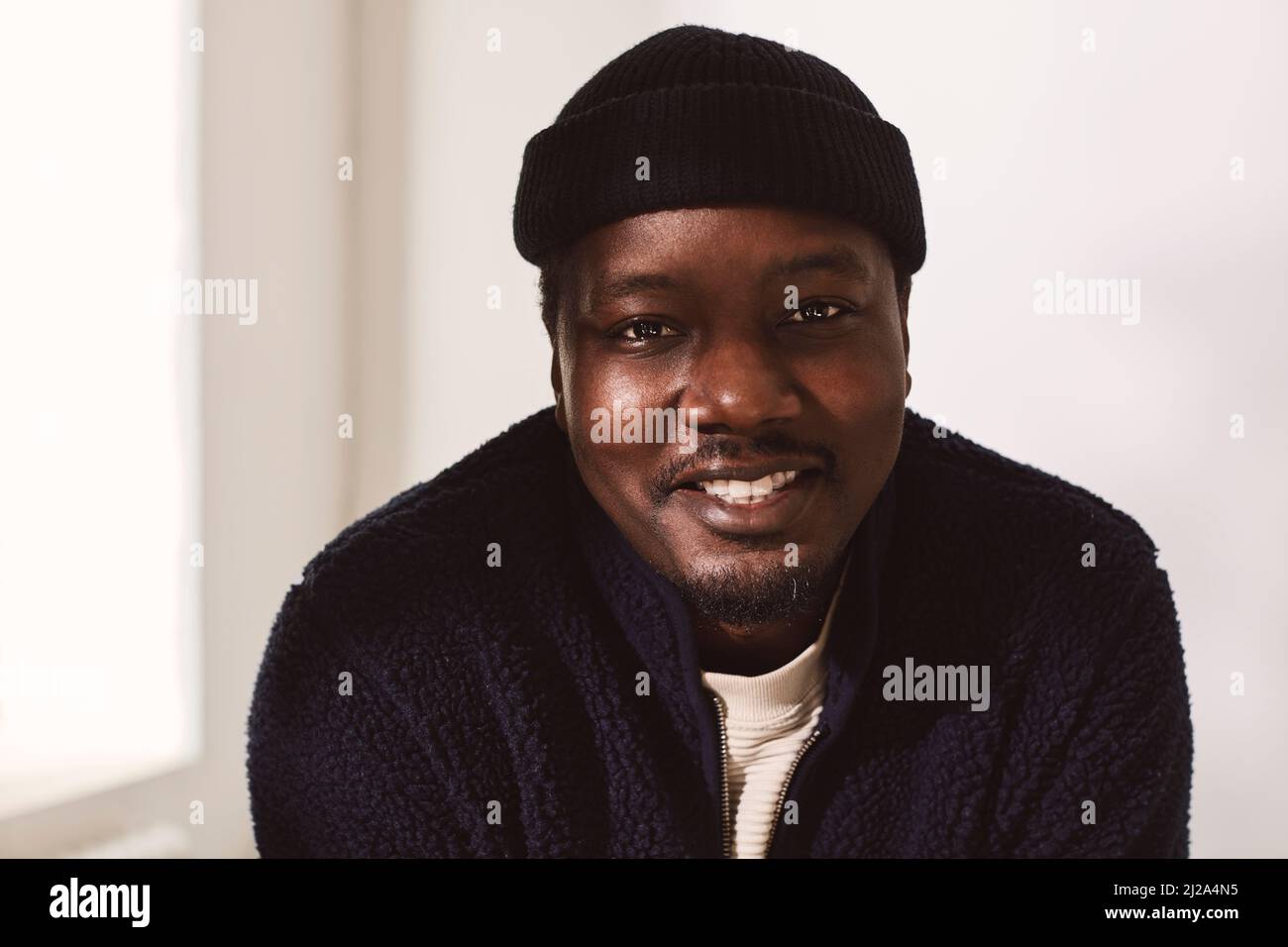 Smiling mid adult man wearing knit hat against wall Stock Photo