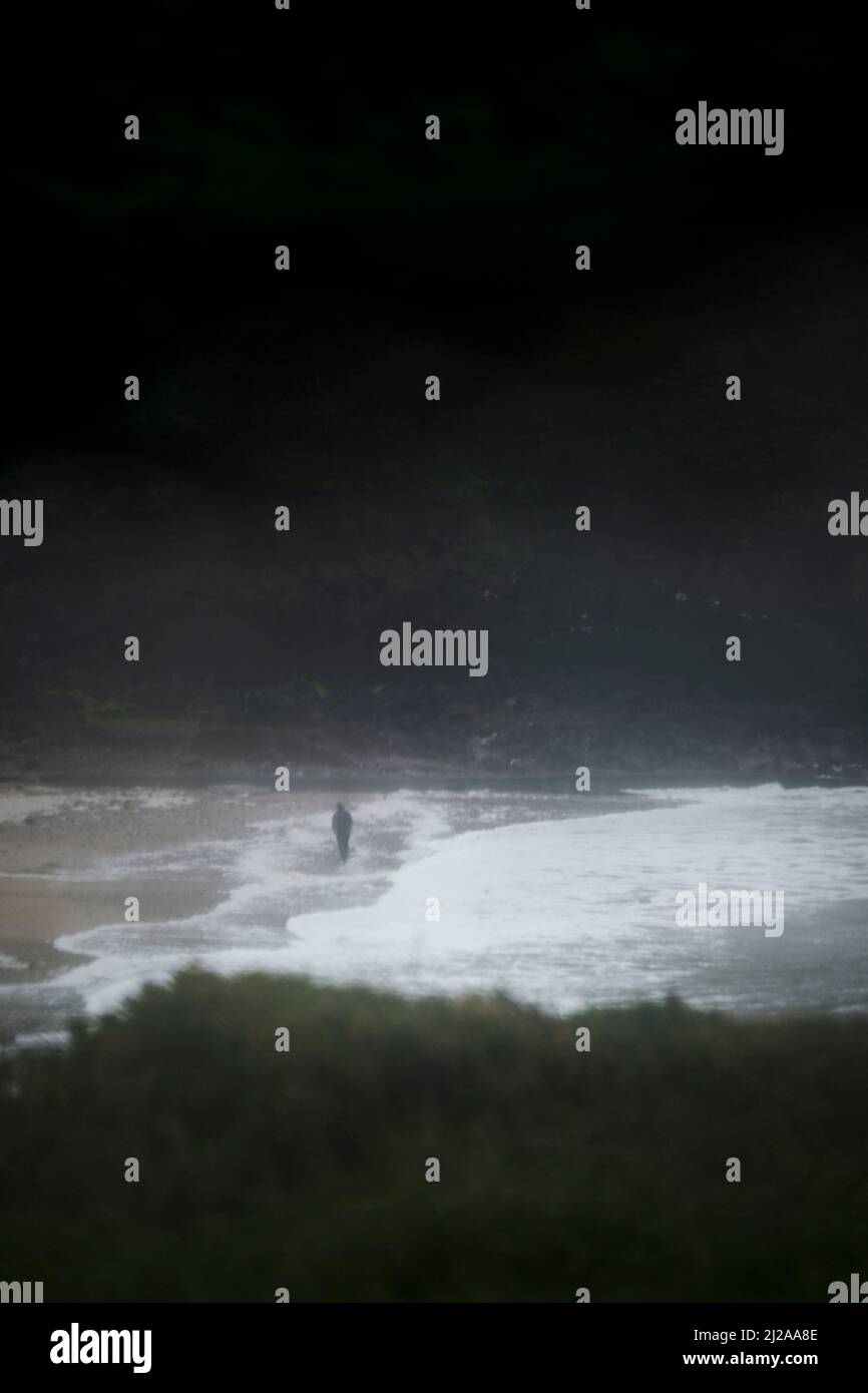 Coastal view through a car window at a wild stormy grey and wet day outside with a tiny silhouetted figure walking on the beach. Stock Photo