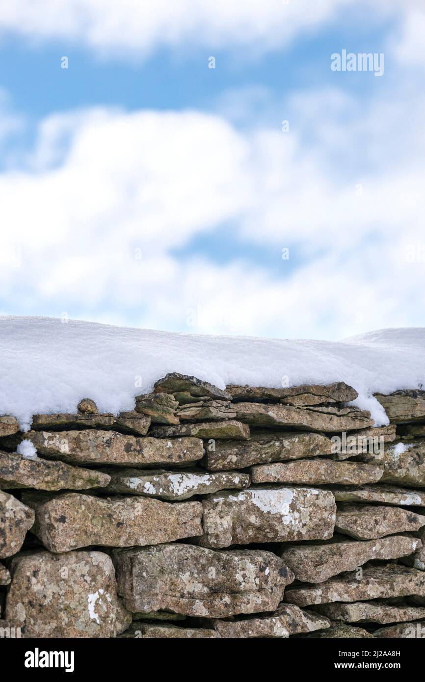 A cotswold stone wall across a framer's field covered in a light fall of snow. Stock Photo