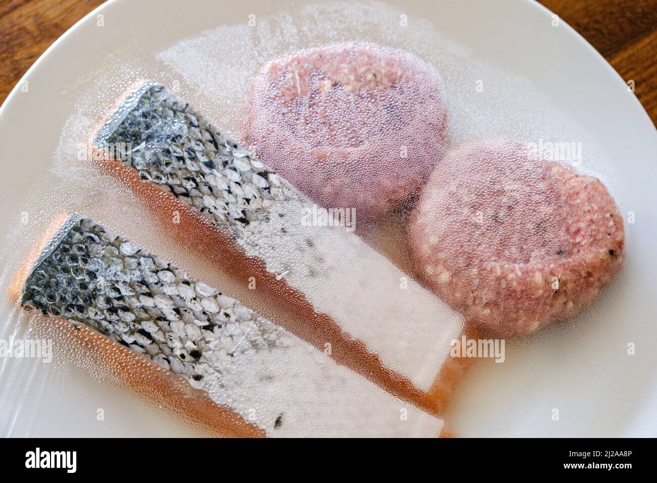 A plate of uncooked food, inclduing salmon fillets and beef burgers ready for a barbecue. Stock Photo
