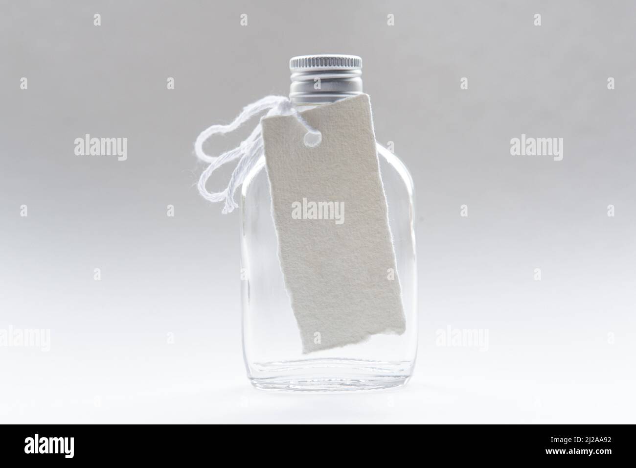 A small glasss bottle with a blank note tied around it's neck shot on shot studio background. Stock Photo