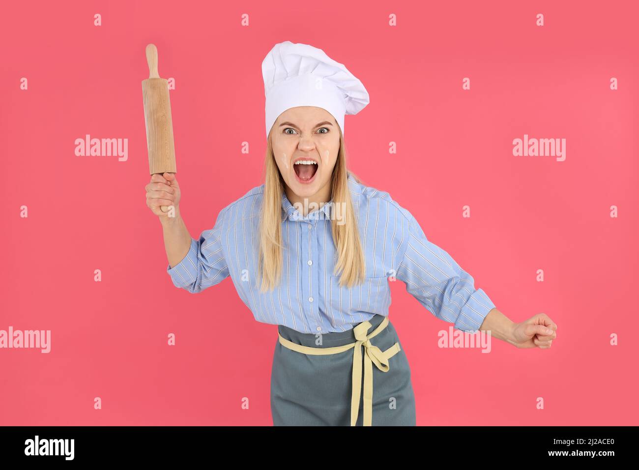Angry woman with rolling pin on pink background Stock Photo