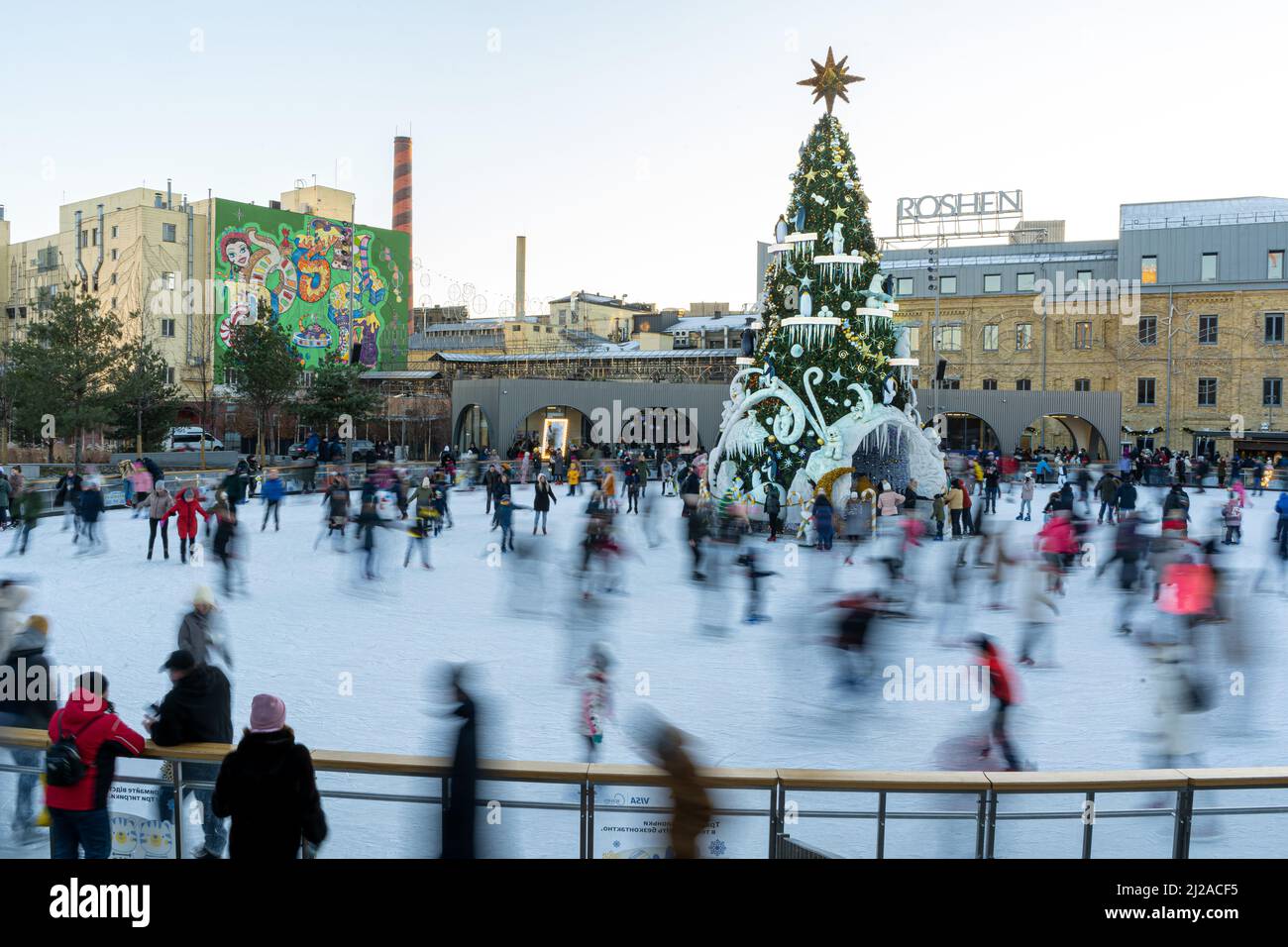 Ukraine, Kyiv - January 7, 2022: Ice skating rink in winter. People are skating. Skates ride on ice. Ice skating is a winter sport entertainment. Christmas time. Christmas tree Roshen factory. Crowd Stock Photo