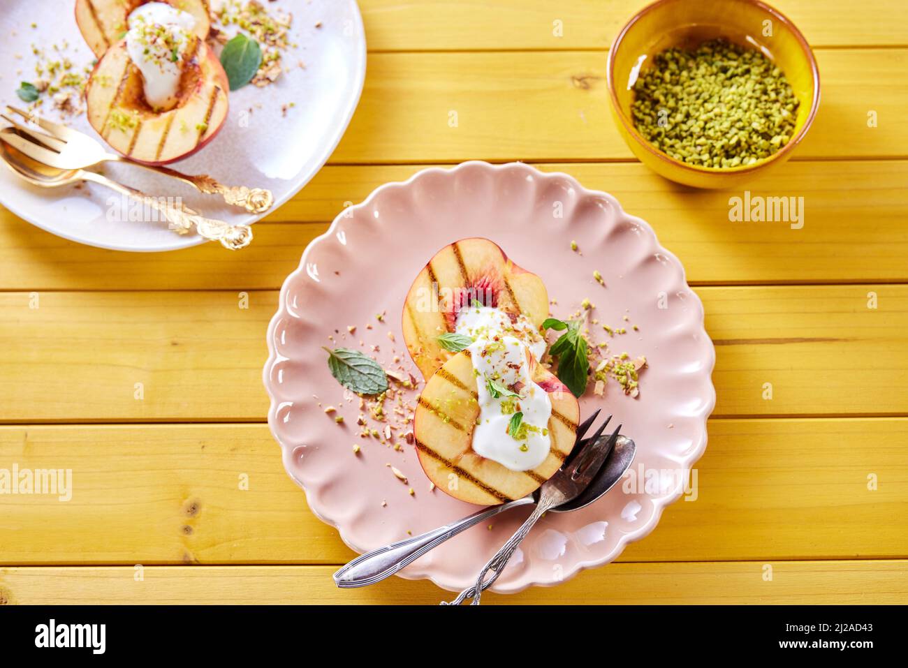 Overhead view of plate with delicious sweet nectarines with yogurt and mint leaves served on wooden table with bowl of pistachios Stock Photo