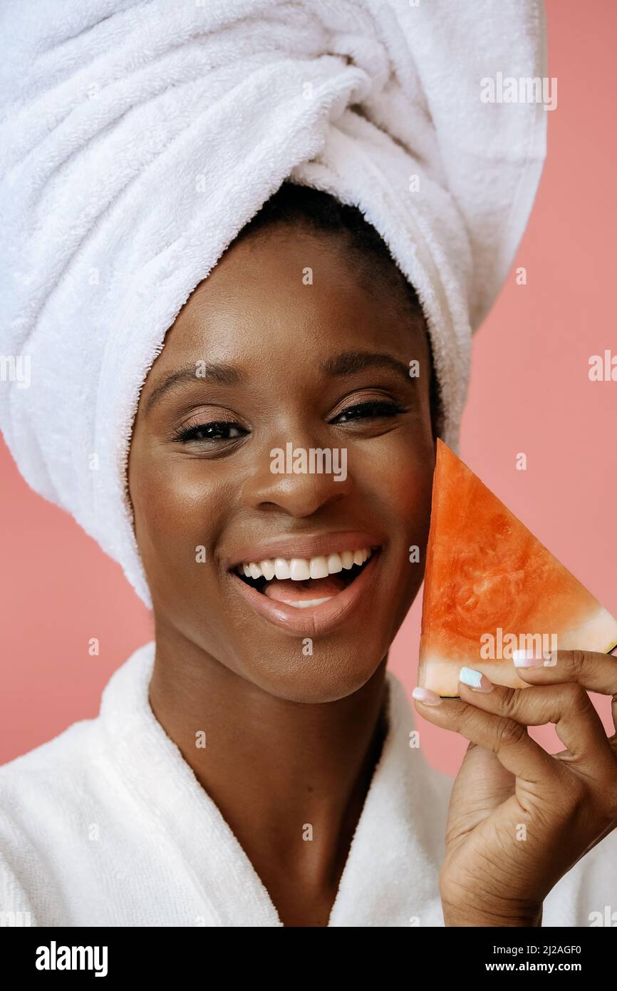 Young beautiful woman smiling with white towel on head holding slice of watermelon on pink background Stock Photo