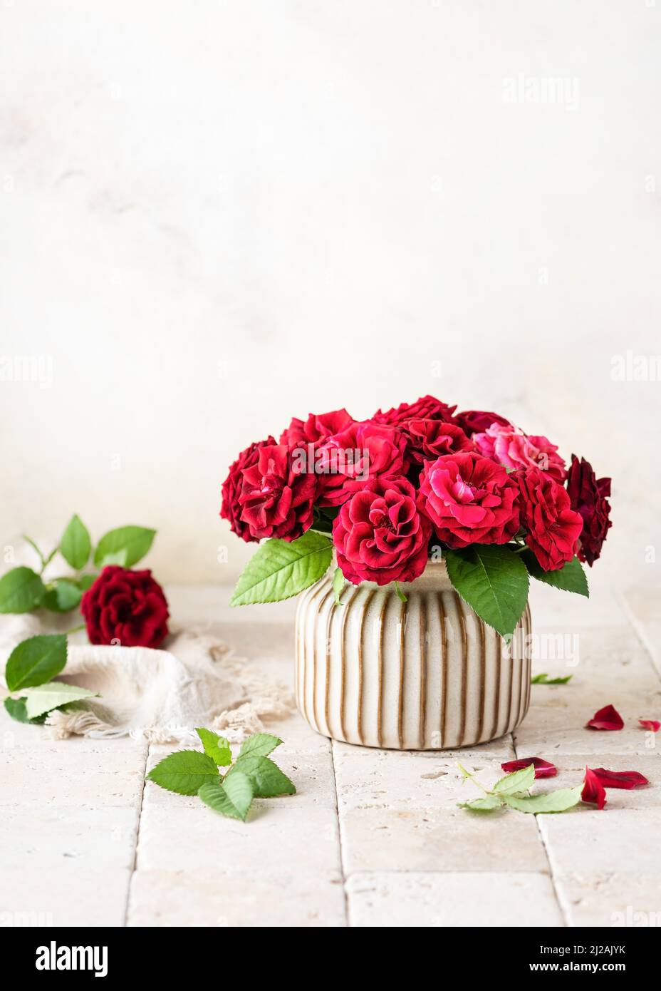 Beautiful bouquet of summer dark red roses in ceramic vase on light stone mosaic background. Floristic or home deco concept. Selective focus. Stock Photo