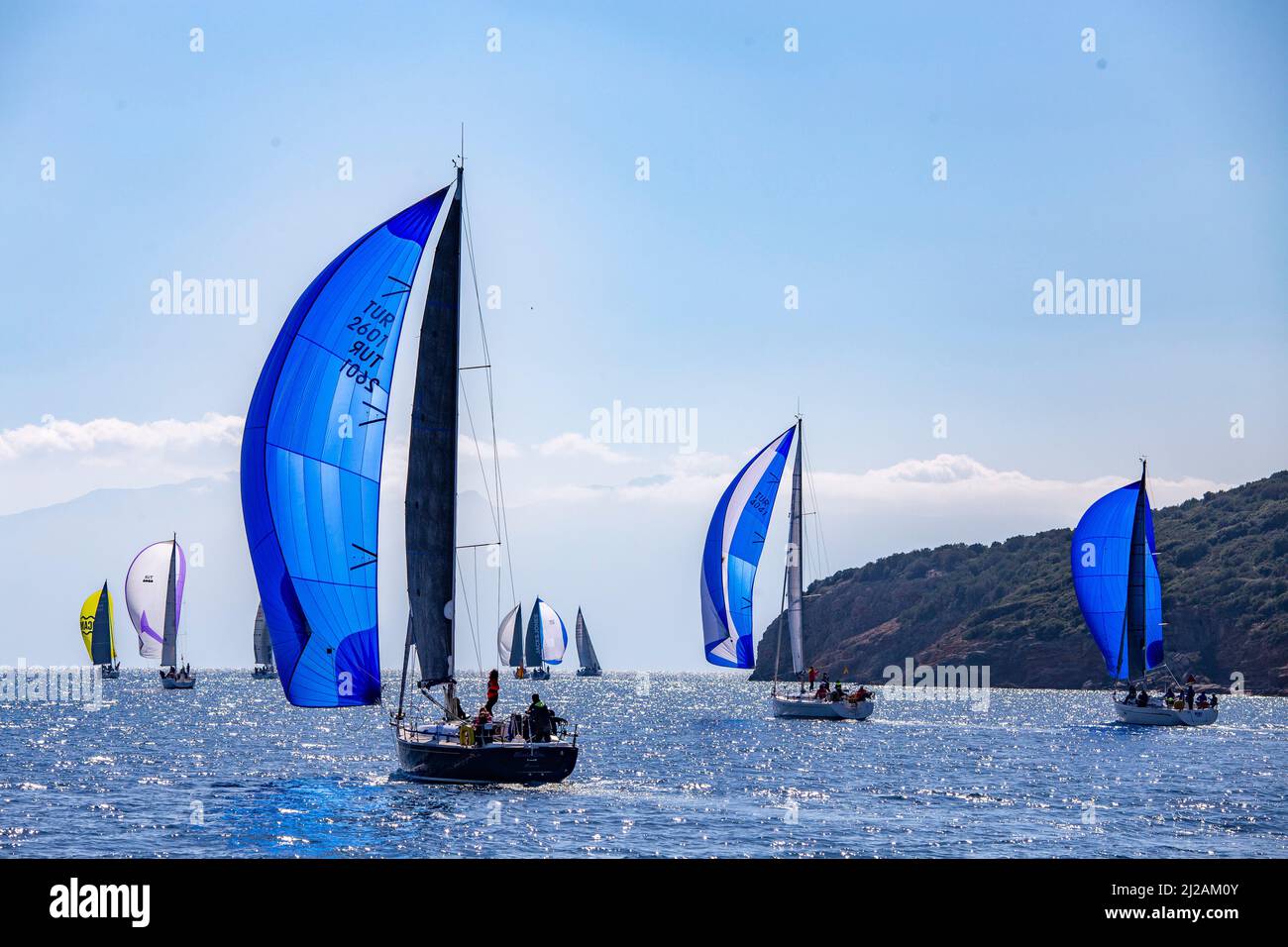 Bodrum, Mugla, Turkey - 02.25.2022: Three in a row Ship yachts with blue sails on shiny waters of Aegean Sea. Sailboats sail in windy weather. Regatta Stock Photo
