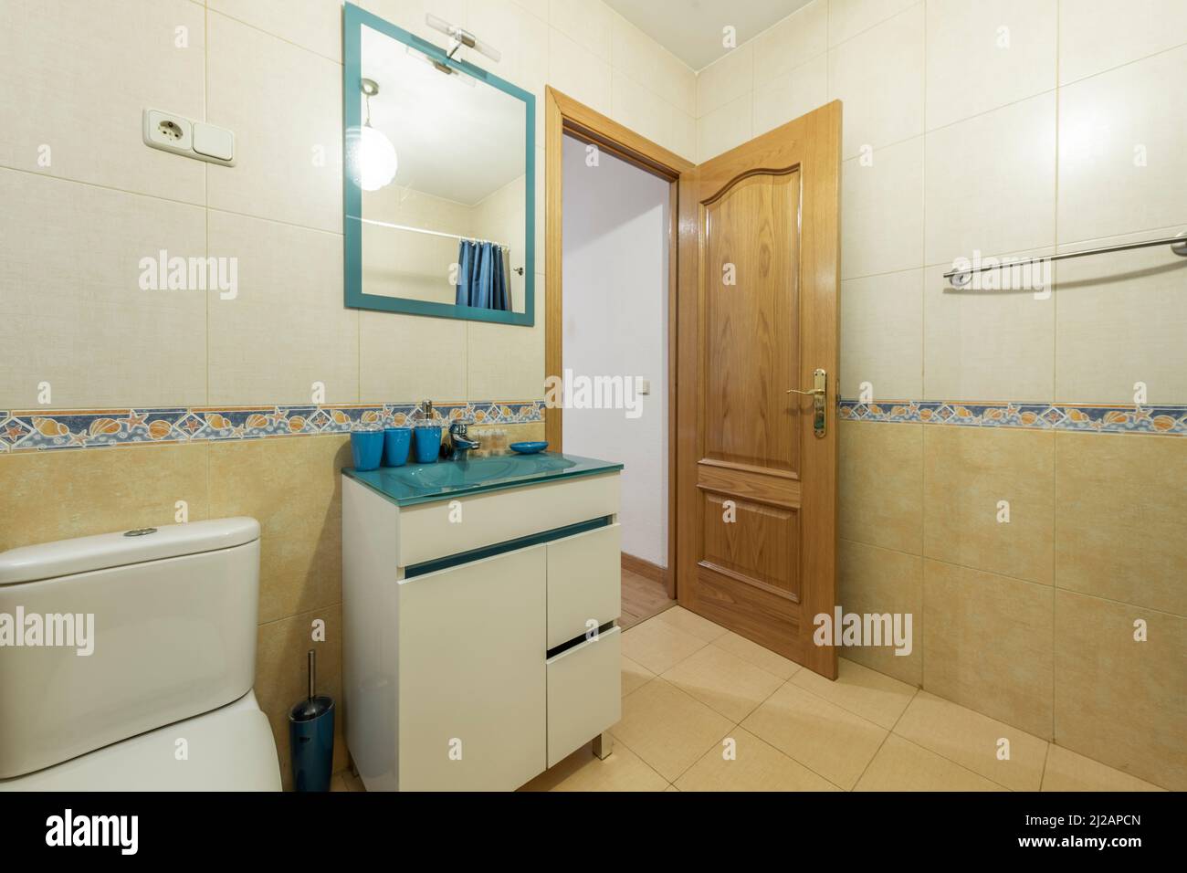 Bathroom with blue glass top vanity, mirror with matching frame and varnished pine wood door with border on the walls Stock Photo