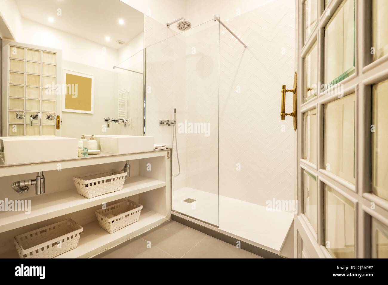 Bathroom with glassenclosed shower stall with white wicker baskets, brick wooden door