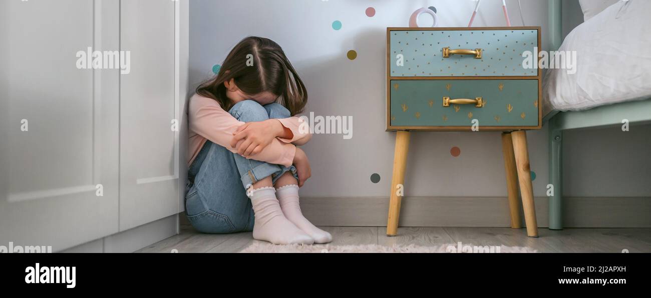 Sad little girl sitting on the floor of her bedroom Stock Photo