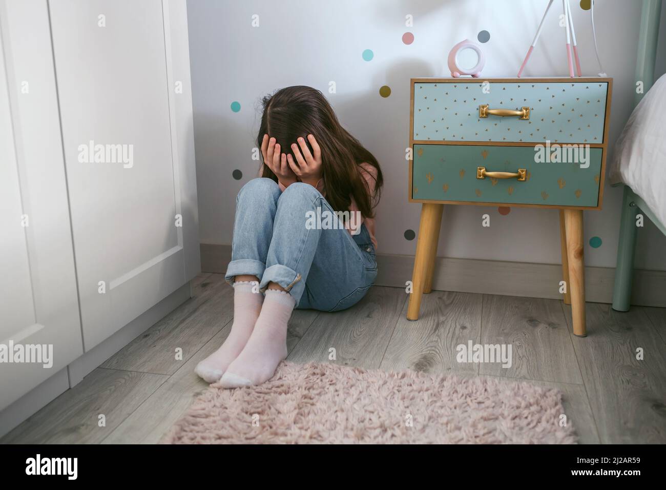 Unrecognizable little girl covering her face with hands sitting on the floor Stock Photo