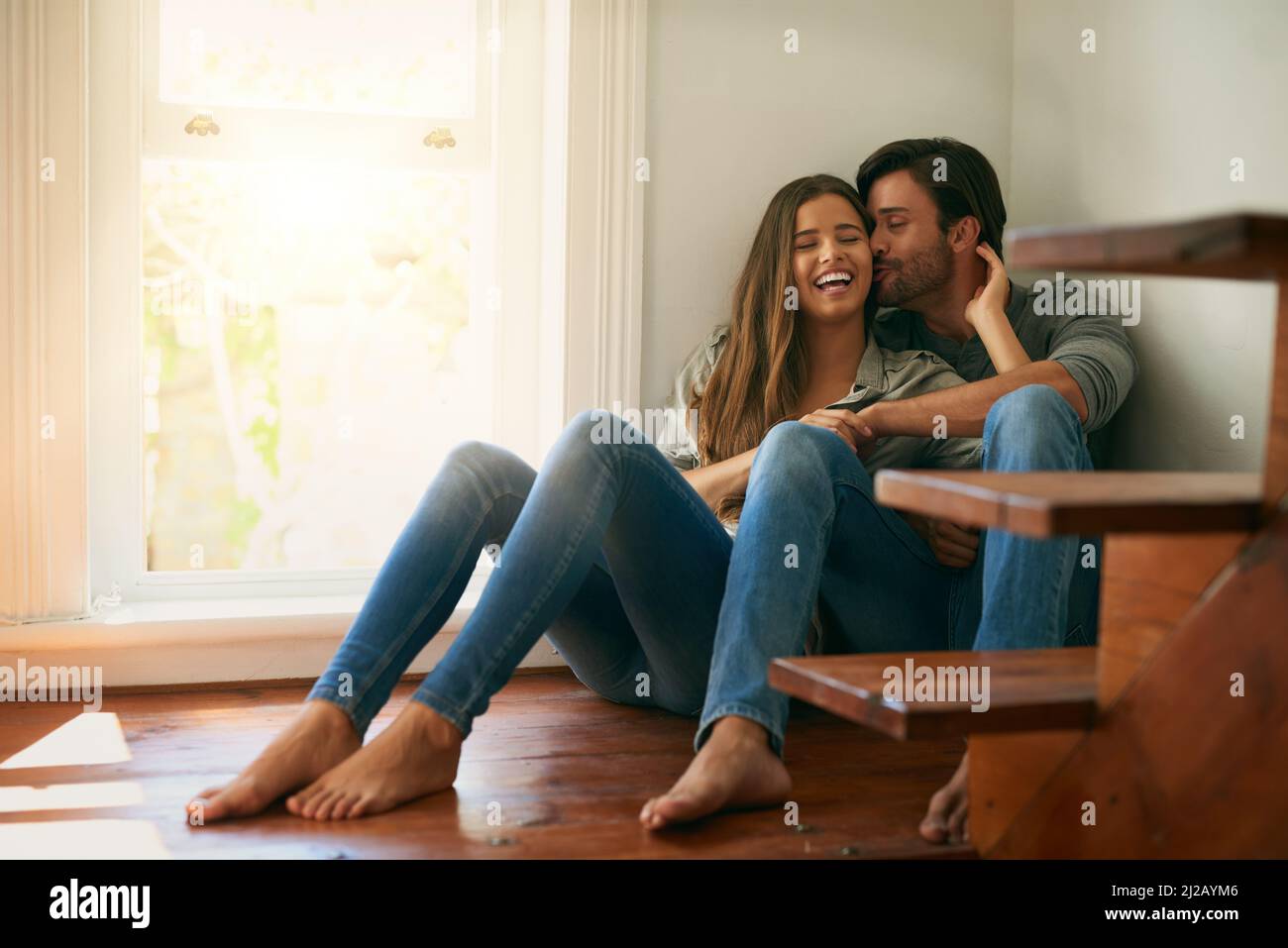 We are both the same in every way. Shot of an affectionate young couple sitting in a corner and holding each other. Stock Photo