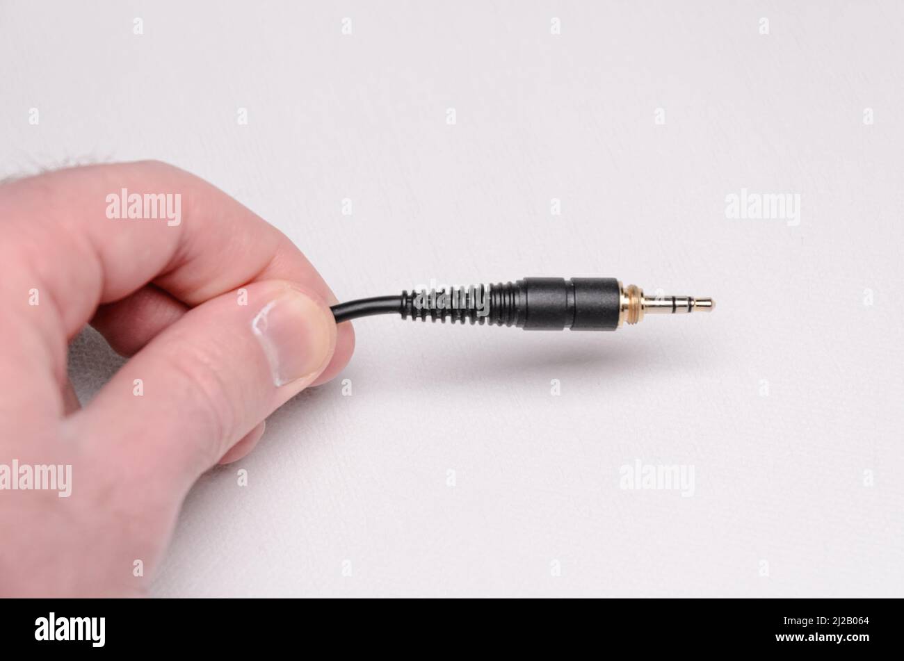 Holding a 3.5mm stereo headphone jack connector and cable for analog audio signals on white background Stock Photo