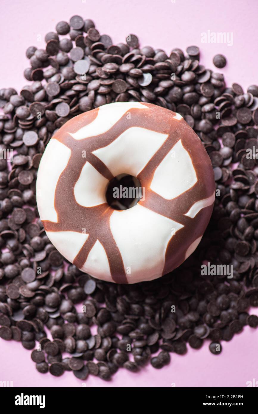 Doughnut with chocolate glaze on a chocolate chips on a pink background. Top view. Stock Photo