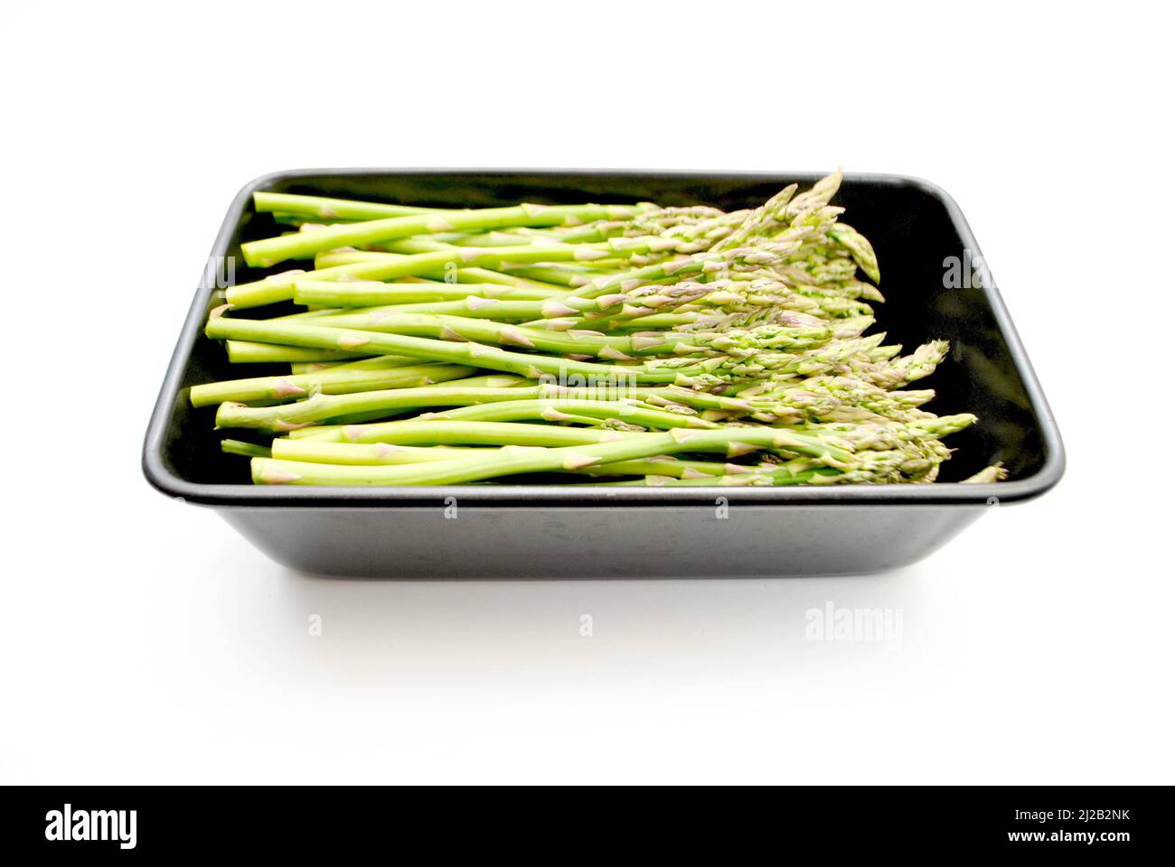 Green Asparagus in a Black Baking Pan Isolated Over a White Background Stock Photo
