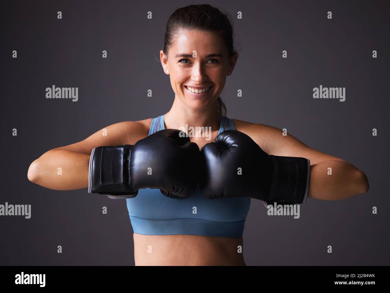 Wanna see how much power are in my punches. Portrait of a young woman wearing boxing gloves against a grey background. Stock Photo
