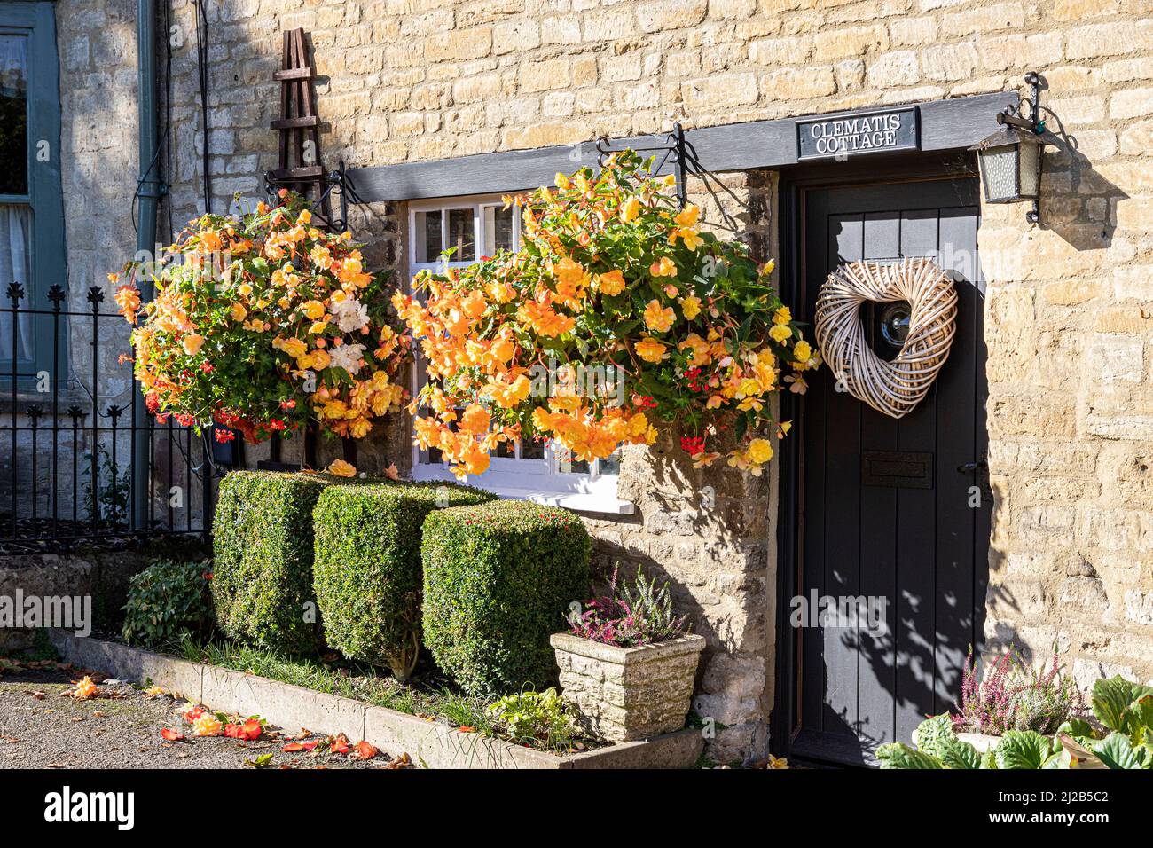 Begonias flowering in hanging baskets outside Clematis Cottage in the Cotswold town of Burford, Oxfordshire, England UK Stock Photo